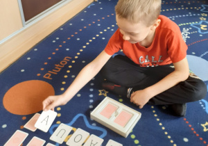 chłopiec siedzi na podłodze, wykonuje zdanie przy pomocy kart literowych