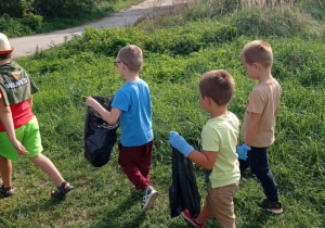 grupa dzieci zbiera śmieci, niektóre z nich mają w dłoniach worki