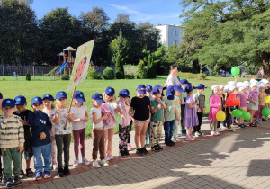 grupa dzieci i nauczycielki zgromadzone na przedszkolnym podwórku, przygotowują się do parady ulicami miasta