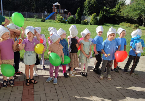 grupa dzieci i nauczycielki zgromadzone na przedszkolnym podwórku, przygotowują się do parady ulicami miasta
