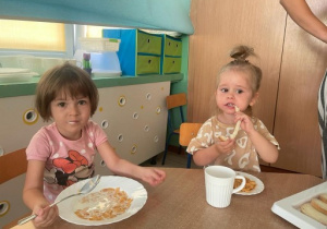 dwie dziewczynki przy stoliku, jedzą śniadanie