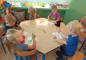grupa dzieci siedzi przy stoliczku i koloruje szablon "ekoludka"