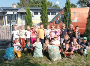 Dzieci z grupy "Biedronki" pozują do zdjęcia. Przed nimi znajdują się zapełnione worki na śmieci.