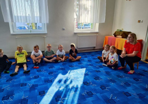 Dzieci z grupy "Biedronki" siedzą w kole na dywanie. Uczestniczą w zajęciach bibliotecznych.