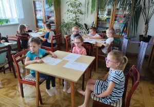 Dzieci siedzą przy stolikach. Przed nimi znajdują się kartki z narysowaną wiewiórką.