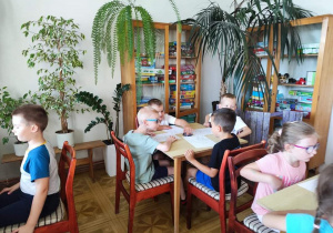 Dzieci siedzą przy stolikach. Przed nimi znajdują się kartki z narysowaną wiewiórką.