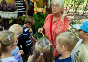 Dzieci słuchają prelekcji Pani Jolanty Siemieńskiej, która prezentuje przedszkolakom kosz z roślinami.