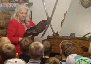 pani B. Kaszyńska pokazuje dzieciom stare przedmioty codziennego użytku zgromadzone w budynku, na ścianach wiszą starodawne przedmioty