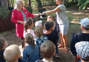 pani B. Kaszyńska podaje nauczycielce koszyczek, wokół stoją dzieci