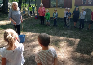 p. B. Kaszyńska pokazuje, jak robić mega bańki mydlane, wokół niej zgromadzone dzieci, na drugim planie budynek