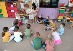 mama jednego z przedszkolaków siedzi na krzesełku i czyta dzieciom, które siedzą wokół niej na dywanie