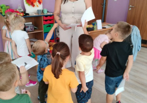 zaproszona na spotkanie mama jednego z przedszkolaków odbiera od dzieci laurki, dzieci stoją wokół niej na dywanie