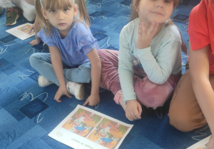 dzieci siedzą na dywanie, oglądają ilustracje