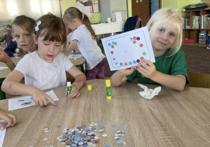 grupa dzieci siedzi przy stoliku, wykonują obrazki z kółek origami