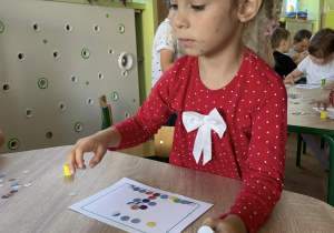 dziewczynka siedzi przy stoliku, wykonują obrazki z kółek origami