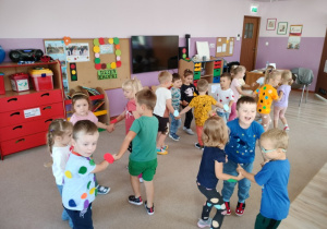 grupa dzieci tańczy w małych zespołach, dzieci mają przyklejone na koszulkach kolorowe kółka