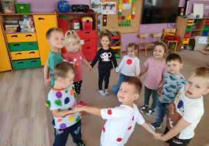 grupa dzieci tańczy , dzieci mają przyklejone na koszulkach kolorowe kółka