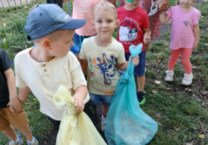 dzieci zbierają śmieci w parku , mają założone rękawiczki jednorazowe, w dłoniach worki na odpady
