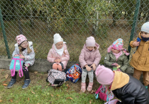grupa dzieci siedzi na murku ogrodzeniowym i zjada posiłek