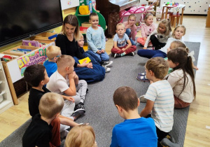 Przedszkolaki wraz z nauczycielką siedzą na dywanie i prowadzą rozmowę.
