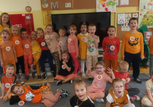 Dzieci z grupy Biedronki i nauczycielka pozują do zdjęcia. Wszyscy ubrani są w pomarańczowe stroje, na szyi mają zawieszone dyniowe medale.