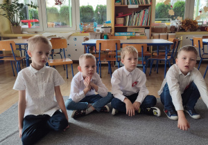 grupa chłopców w białych koszulach siedzi na dywanie w klasie