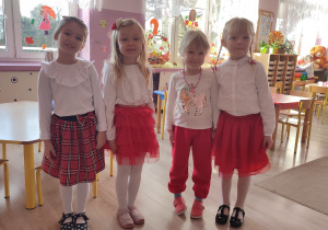 cztery dziewczynki stoją razem, mają białe bluzeczki i czerwone spódniczki