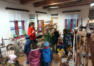 grupa dzieci w muzeum, słuchają pani przewodniczki opowiadającej o historii zgierskich tkaczy