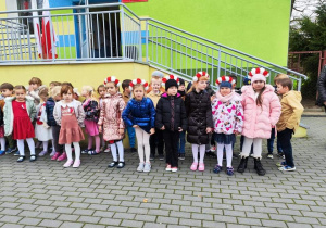 dzieci stoja przed budynkiem przedszkola, przygotowują się do zaśpiewania hymnu