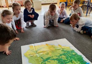 grupa dzieci siedzi na dywanie w klasie, przed nimi na dywanie leży mapa Polski
