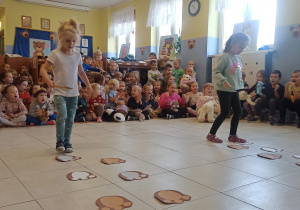 dwie dziewczynki biorą udział w zabawach sprawnościowych, w tle siedzą dzieci