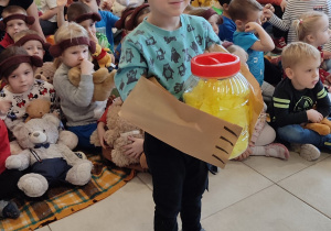chłopiec bierze udział w zabawie sprawnościowej, na dłonie ma założone papierowe torebki - atrapy misiowych łapek, w tle siedzą dzieci