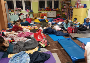 grupa dzieci w klasie, rozłożone karimaty i śpiwory, szykują się do snu
