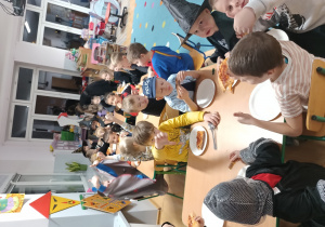 grupa dzieci przy stolikach w klasie, jedzą pizzę