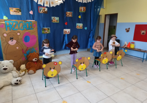cztery dziewczynki biorą udział w zabawach sprawnościowych, przed nimi stoją krzesełka, na nich naklejone tekturowe głowy misiów,