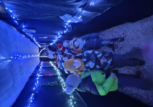 grupa dzieci przechodzi przez tunel wykonany z tkaniny, na ścianach powieszone są ozdoby świąteczne , światełka