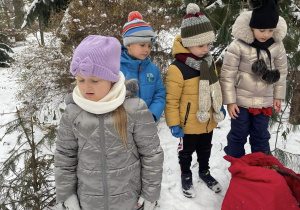 grupa dzieci w przedszkolnym ogrodzie z odnalezionym czerwonym workiem z prezentami, pochylają się nad nim