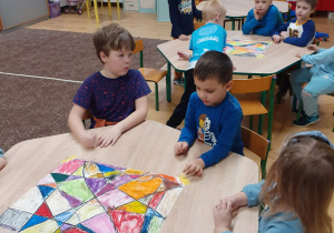 dzieci przy stolikach tworzą wspólnie kartę zabawy "witraż"