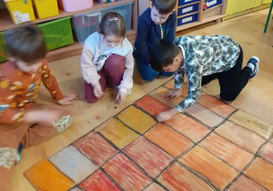grupa dzieci w klasie, kucają na podłodze, tworzą wspólnie wielkoformatową kartę zabawy "kominek Mikołaja"