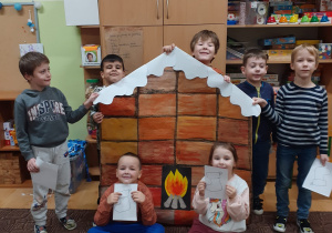 grupa dzieci pozuje do zdjęcia w klasie, w rękach trzymają wielką kartę zabawy "kominek Mikołaja"