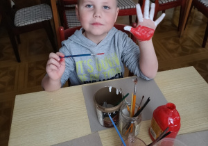 chłopiec pokazuje pomalowaną farbami dłoń - przygotowuje się do odbicia jej na kartce