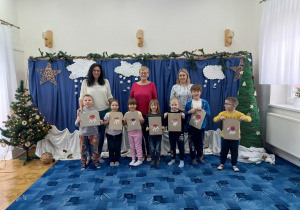 grupa dzieci i nauczycielki pozują do wspólnego zdjęcia , za nimi dekoracja zimowa w bibliotece dla dzieci
