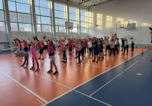 duża grupa dzieci zgromadzona na sali gimnastycznej w SP2 bierze udział w rozgrzewce przed zawodami
