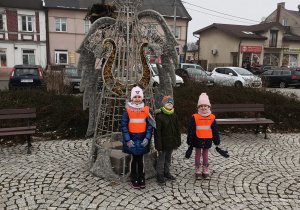 trójka dzieci pozuje do zdjęcia na tle świątecznej dekoracji miejskiej