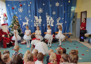 dziewczynki przebrane za śnieżynki tańczą, obok siedzi Mikołaj