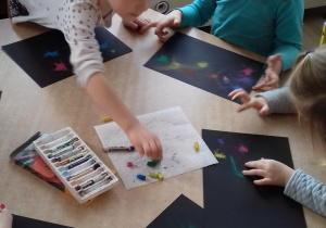 dziewczynki siedzą przy stole i rozcierają pastele na czarnej kartce