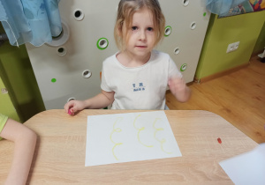 dziewczynka siedzi przy stoliku i kreśli pastelami na karcie zabawy pętle