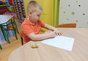 chłopiec siedzi przy stoliku i kreśli pastelami na karcie zabawy pętle