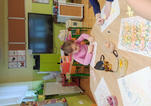 dziewczynka siedzi przy stoliku i kreśli pastelami na karcie zabawy pętle