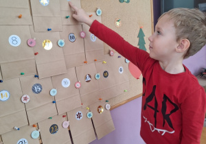 Chłopiec wskazuje okienko z kalendarza adwentowego, na którym znajduje się cyfra 6.